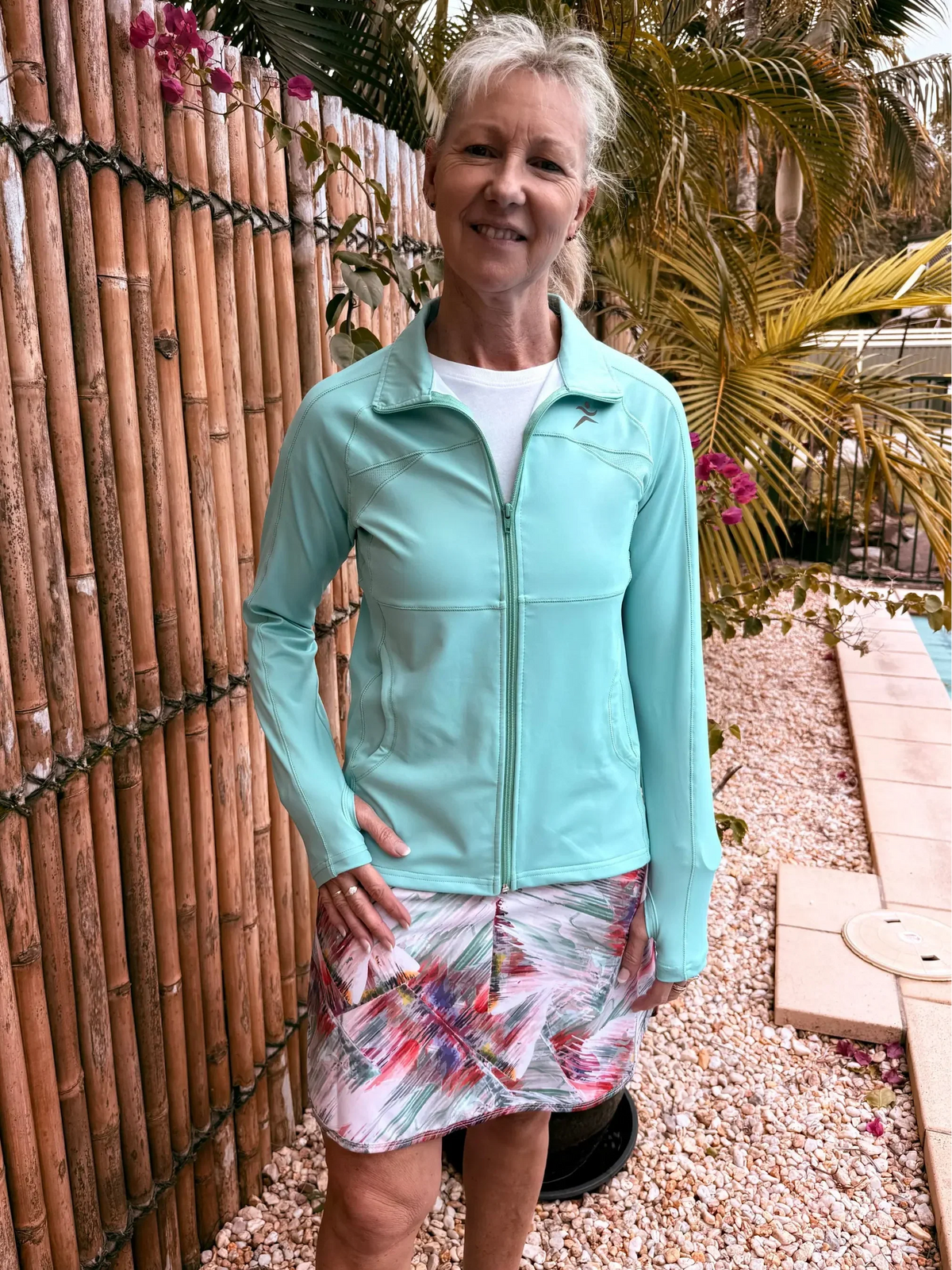 A woman wears a light blue long-sleeved zip-up activewear top with subtle stitching from the Toni Collection.