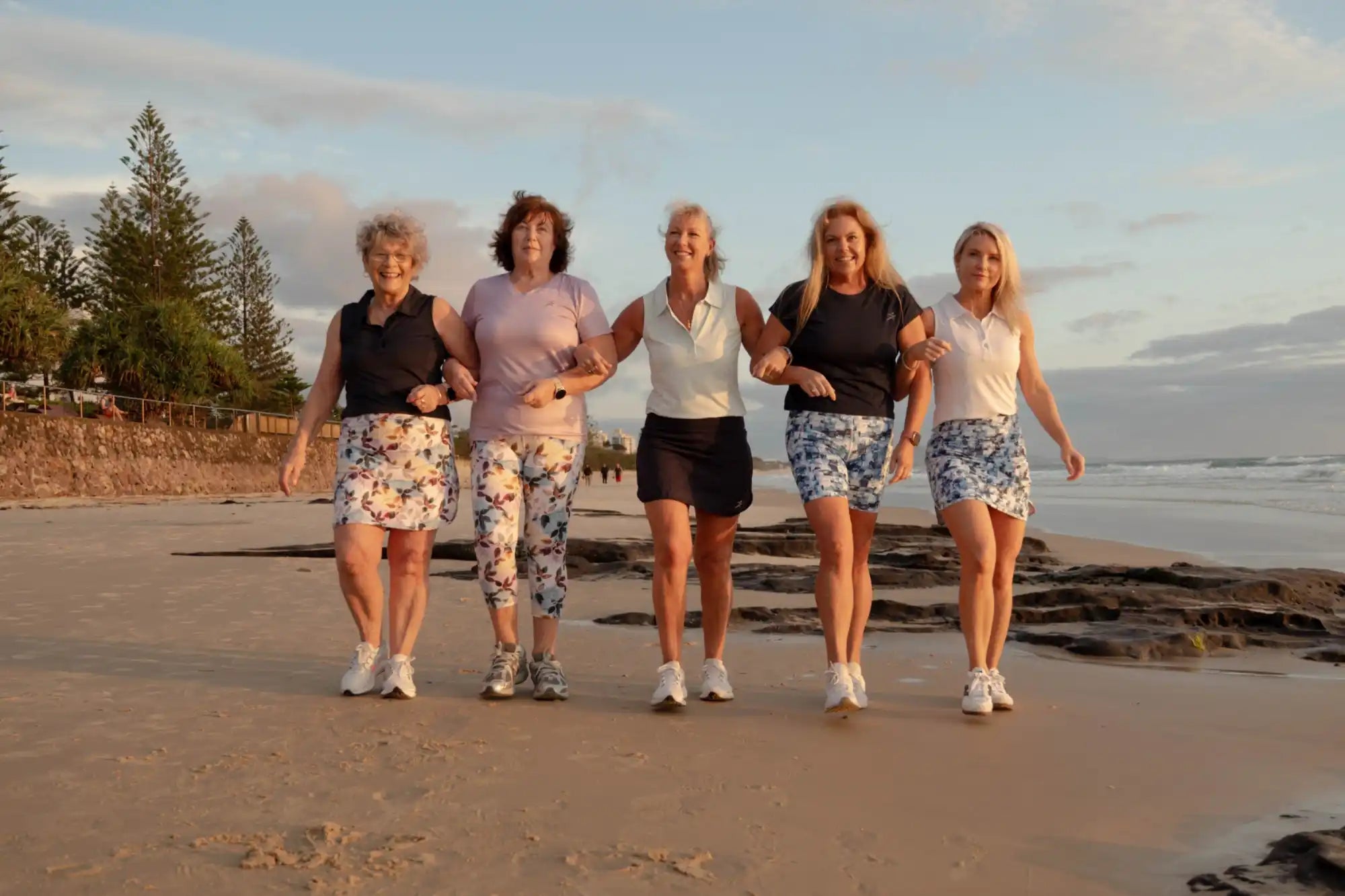 Five women walking on a beach with a scenic background