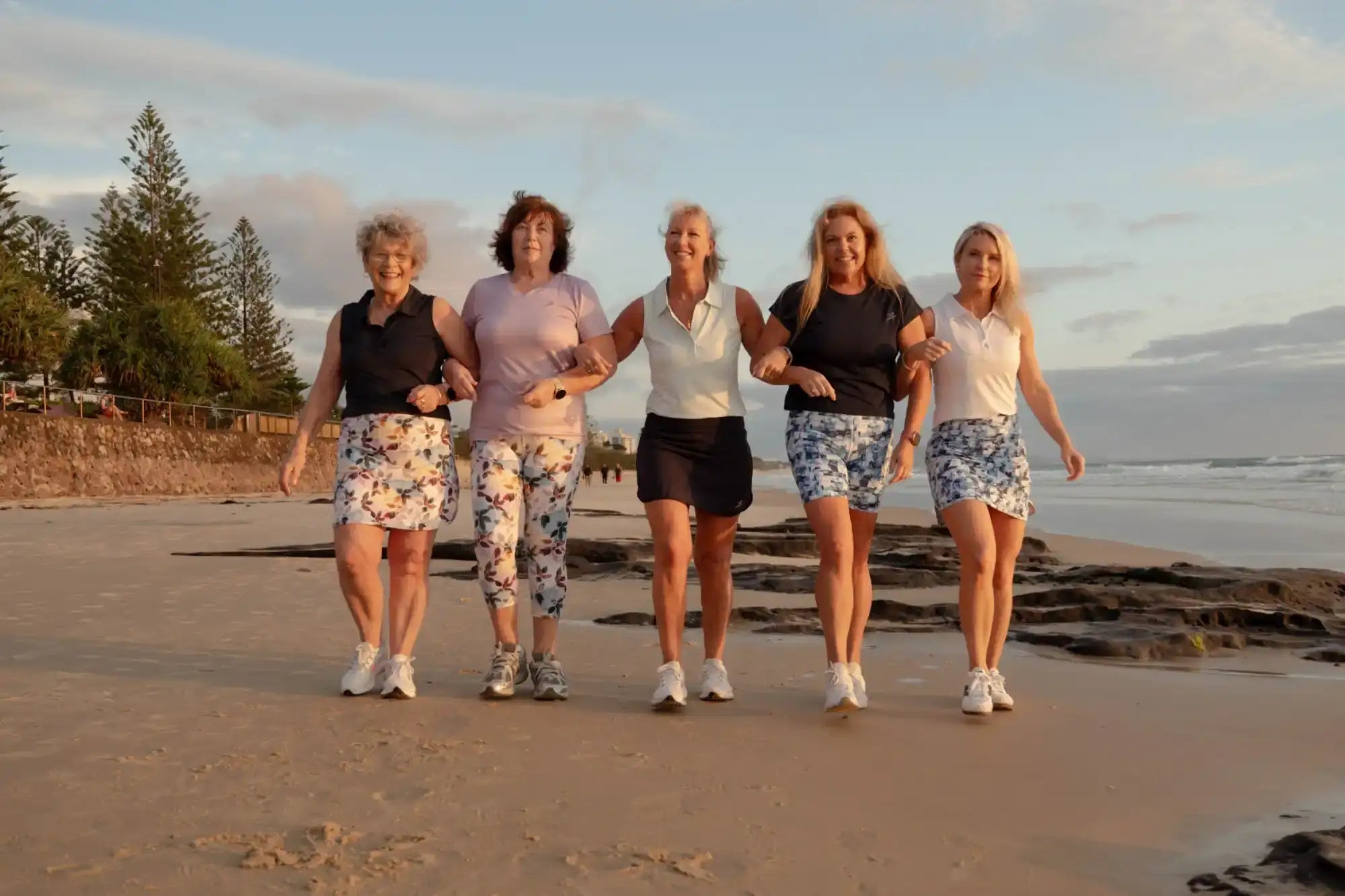 Five women walking on a beach with a scenic background