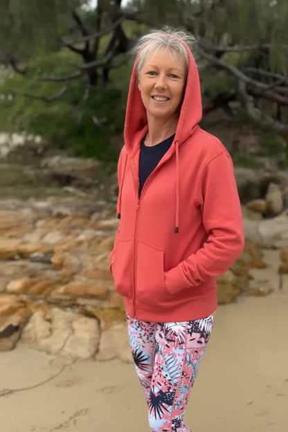 A coral-red fleecy zip hoodie with hood and front pockets worn over a dark blue top perfect for casual wear