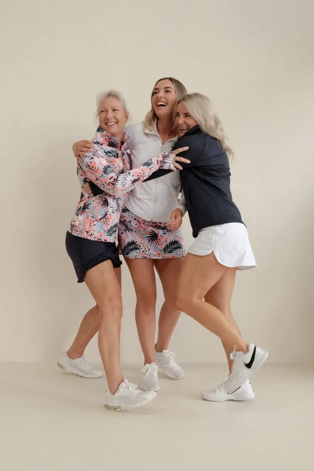Three women wear remi navy sports jackets with vibrant pink and green tropical leaf patterns for golfing