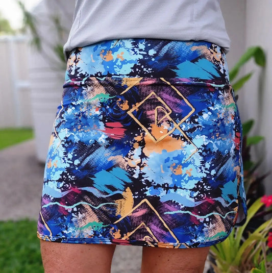 A vibrant sunny skort with pockets featuring bold blue purple and gold abstract patterns and a high-waisted elastic band
