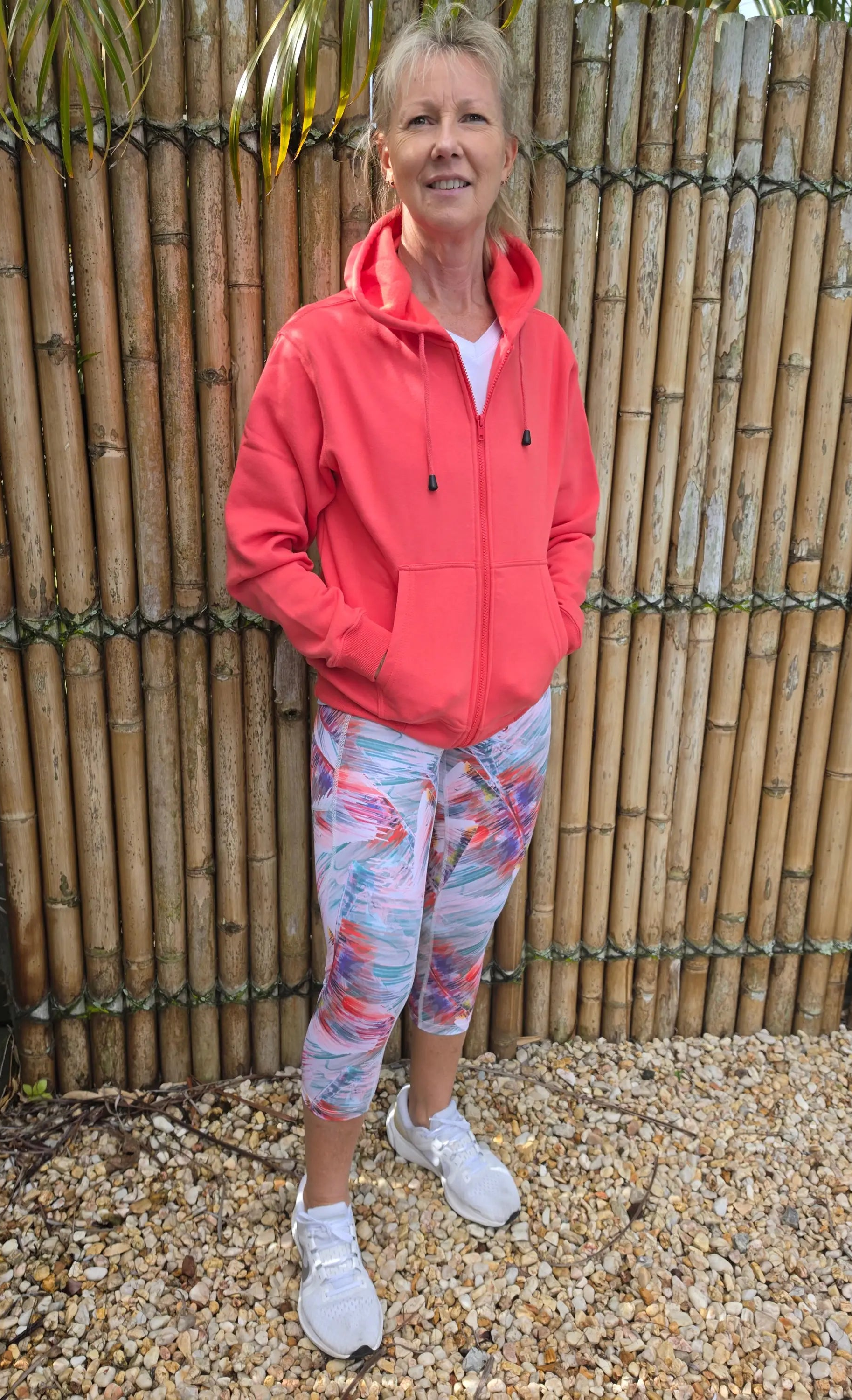 Coral-colored zip-up hoodie with hood and pockets worn over white top paired with moisture wicking active leggings