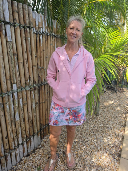 Pink zip-up hoodie with hood and front pockets worn over light shirt paired with cara longer length skort with pockets