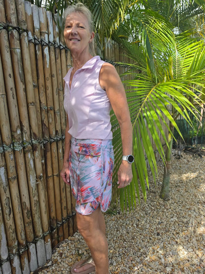 A woman wearing a cara longer skort in light pink sleeveless top with colorful tropical print shorts visible underneath