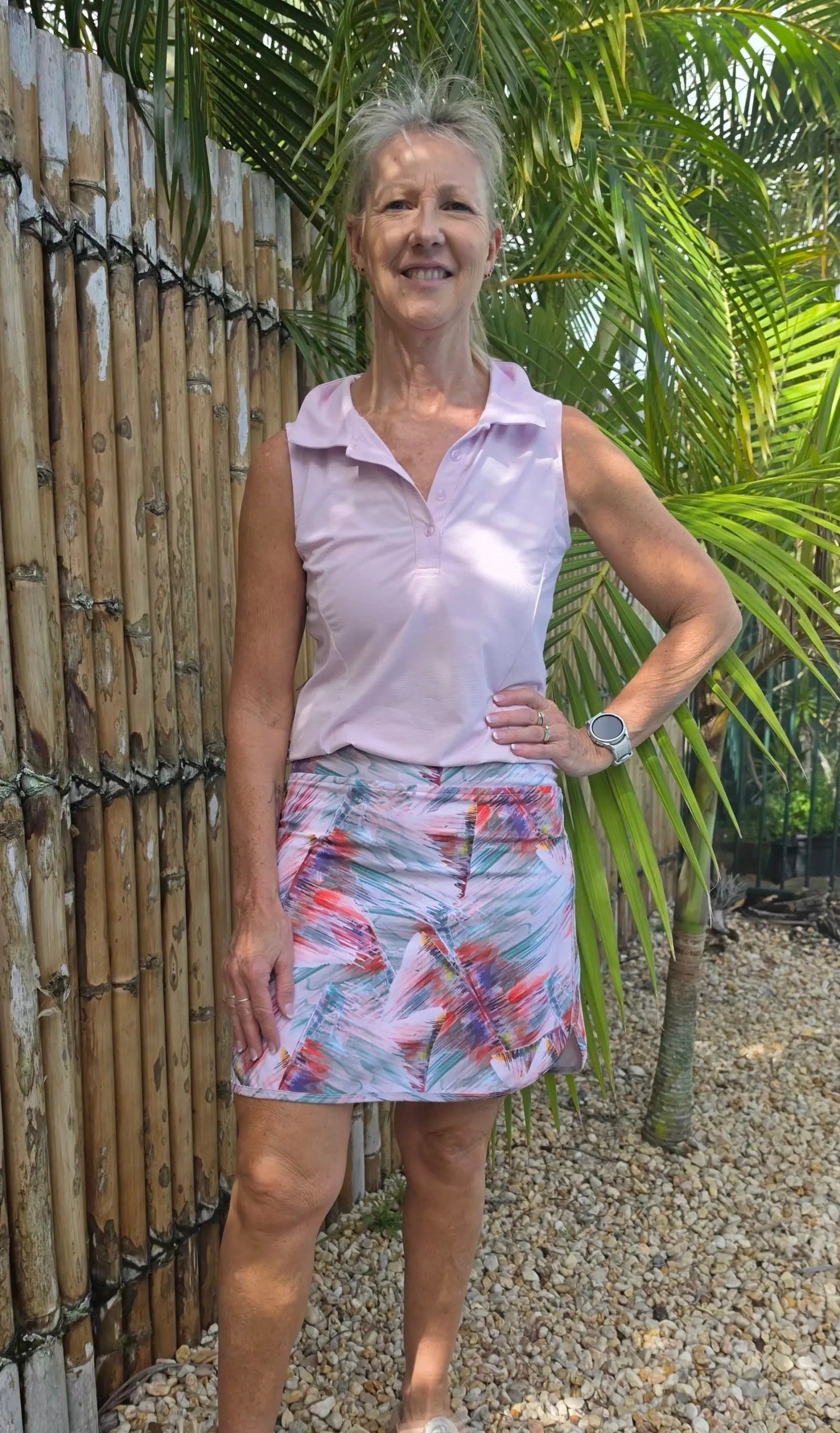 A woman wearing a colorful abstract patterned cara longer skort paired with a light purple sleeveless polo shirt