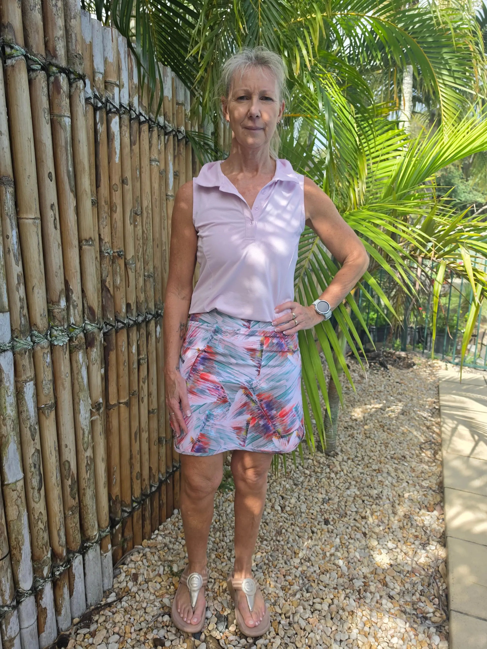 A woman wears a sleeveless lavender polo shirt with a colorful cara longer length skort featuring pockets in xs to 3xl
