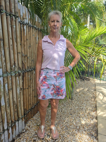 A woman wears a sleeveless lavender polo shirt with a colorful cara longer length skort featuring pockets in xs to 3xl