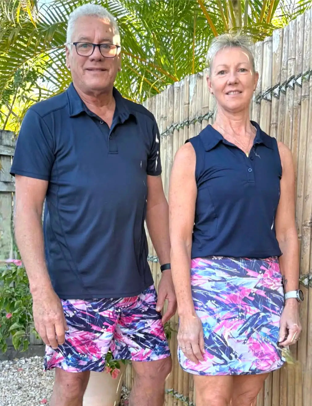 The woman wears a navy blue sleeveless polo shirt paired with a vibrant pink, purple, and white leaf-patterned skirt.